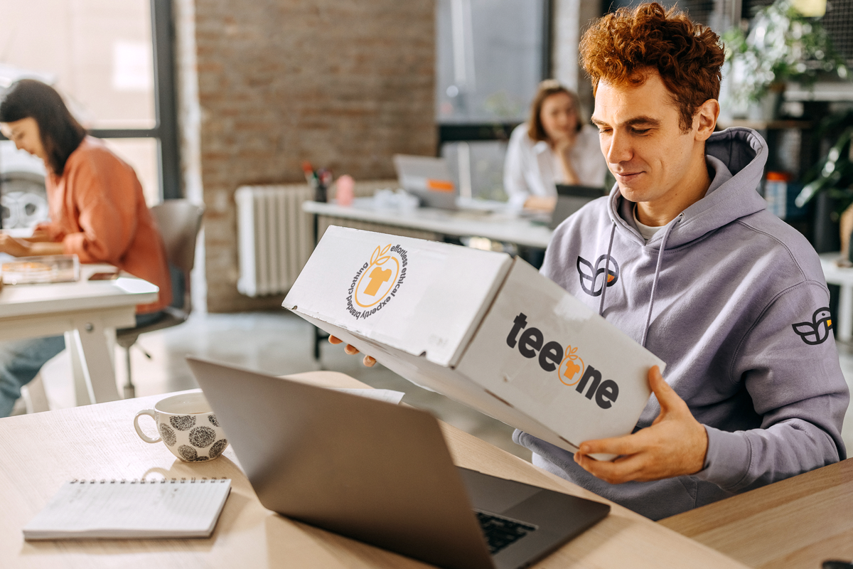 Man in an office excitedly opening his box of sustainable garment samples from Teeone.